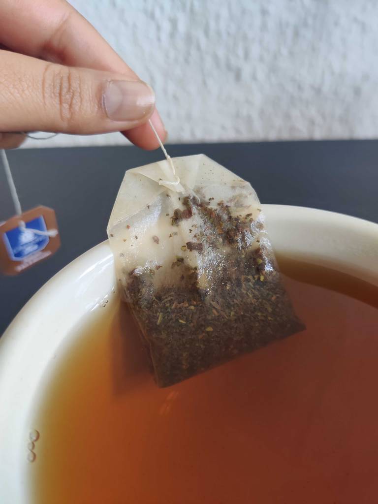 Darjeeling-Tee-Test: Zwei Finger halten einen Teebeutel in eine Tasse mit Flüssigkeit.