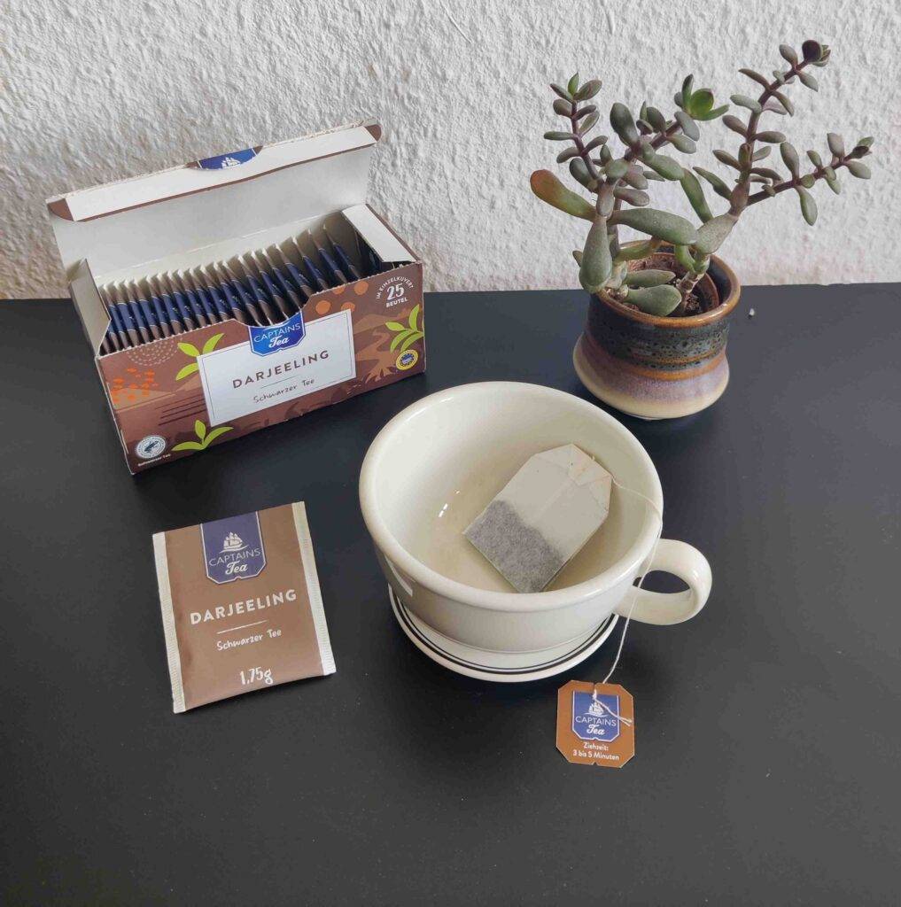 Getestet: Darjeeling-Tee in einem Teebeutel in einer leeren Tasse neben der 25-Beutel-Verpackung.