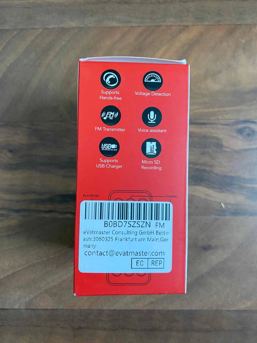 Rote Originalverpackung eines getesteten Bluetooth-Adapters für das Auto, vertrieben von der Evatmaster aus Frankfurt am Main, auf einem Holzuntergrund.