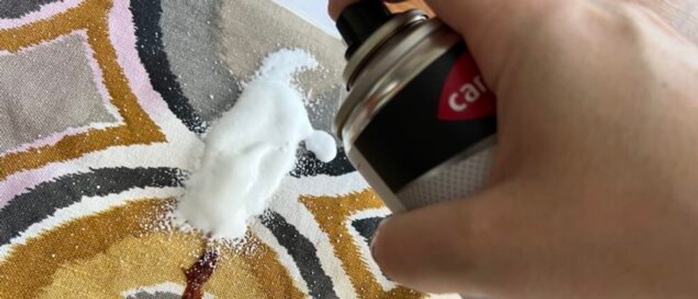 Eine Hand sprüht etwas Caramba 640112 Polsterreiniger auf einen Ketchupfleck.