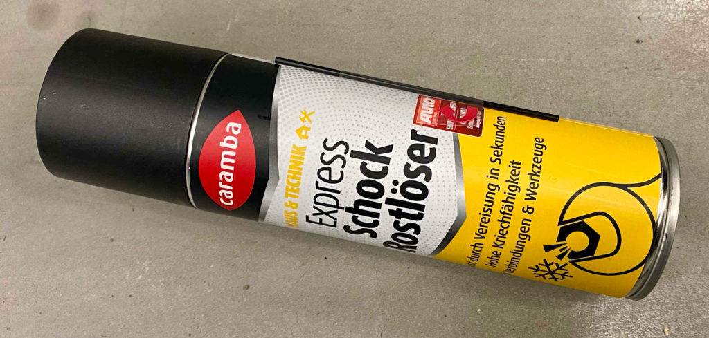 Rostlöser im Test: Caramba Express Schock Rostlöser in einer Sprühdose, mit Fokus auf die seitlich befestigte schwarze Sprühverlängerung für enge Stellen.