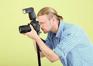 Handsome photographer with camera on monopod, on green backgroun