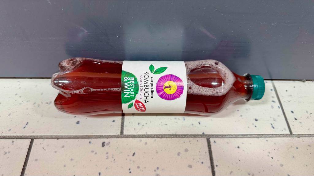 Getesteter Kombucha: Eine transparente Flasche mit roter Flüssigkeit liegt auf dem Boden.