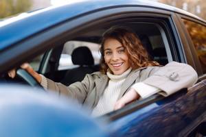 Carsharing-Test: Eine Frau mit lockigen Haaren sitzt am Steuer eines Wagens und lächelt.