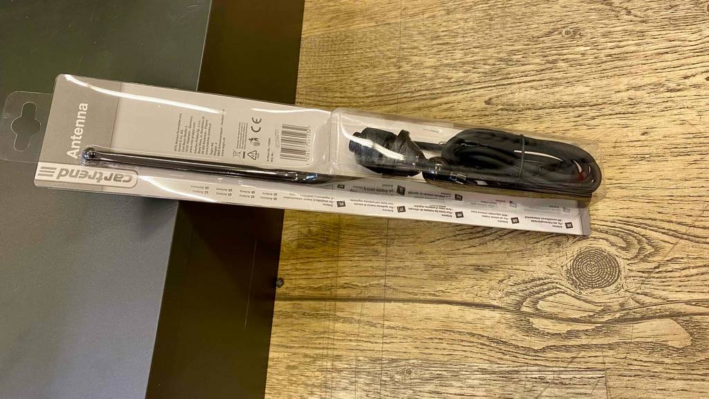 Im Test: eine Autoantenne in Schwarz in ihrer transparenten Verpackung befindet sich auf einer Holzfläche.