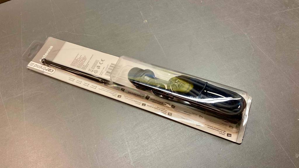 Eine Originalverpackung mit eingeschweißter getesteter Autoantenne liegt auf einer grauen Oberfläche.