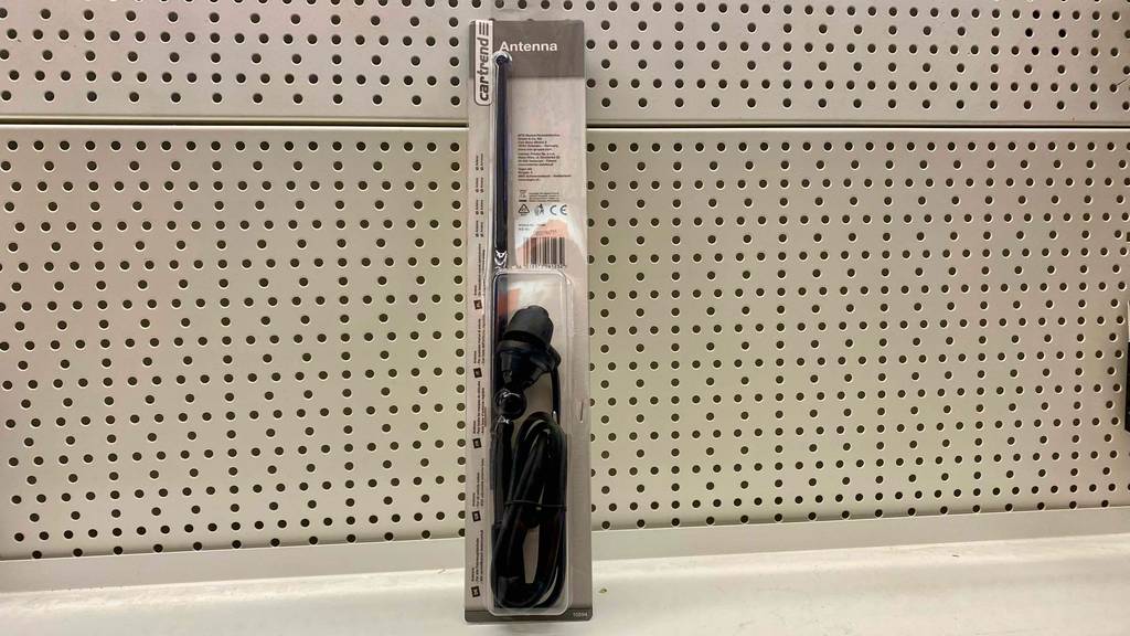 Autoantennen-Test: ein in der transparenten Verpackung verschweißte schwarze Autoantenne lehnt an einer weißen Lochwand.