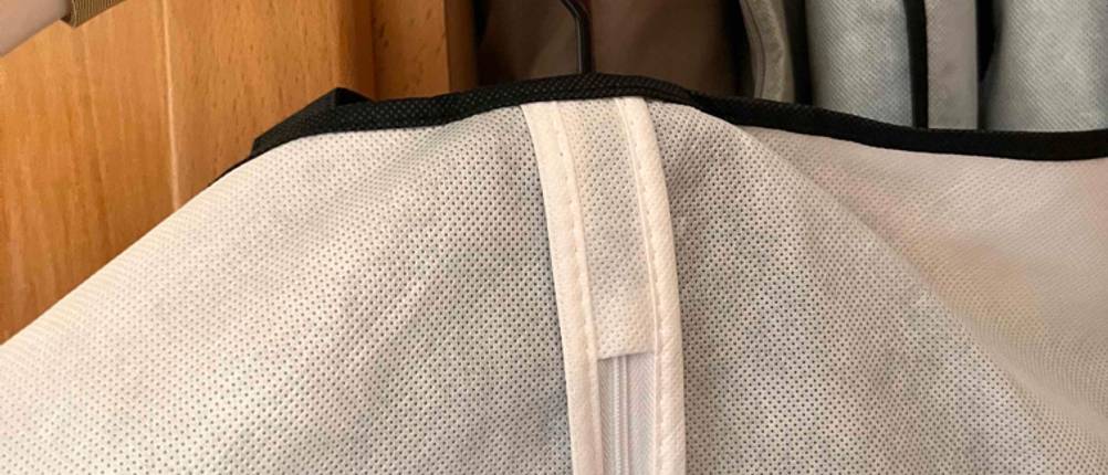Kleidersack-Test: eine Hand hält einen Bügel mit einem Kleidersack darauf vor einem Schrank
