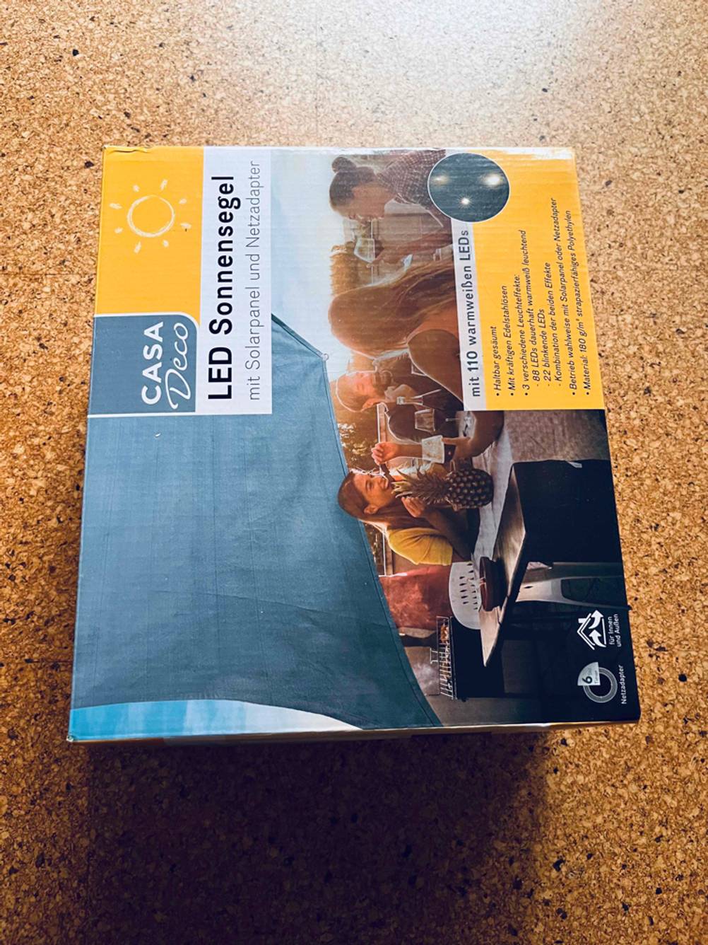 Sonnensegel im Test: Ein verpacktes Sonnensegel von Casa Deko liegt auf einem Korkboden.