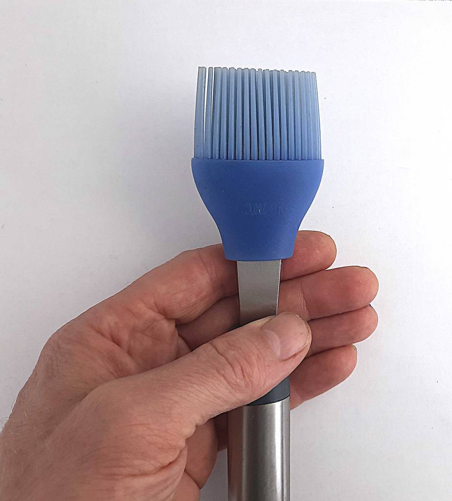 Eine Hand hält den getesteten Grillpinsel mit violettfarbenem Silikon-Kopf an seinem Aluminium-Griff in die Kamera.