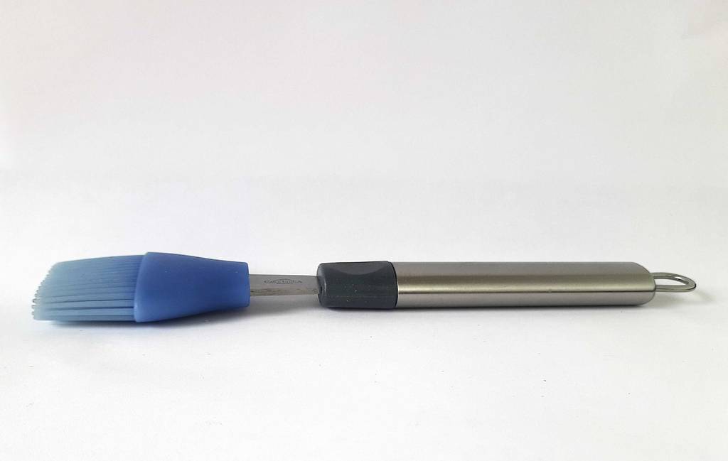 Ein getesteter Grillpinsel mit violettfarbenem Silikon-Kopf und einem Aluminium-Griff liegt von der Seite betrachtet auf einer weißen Oberfläche.