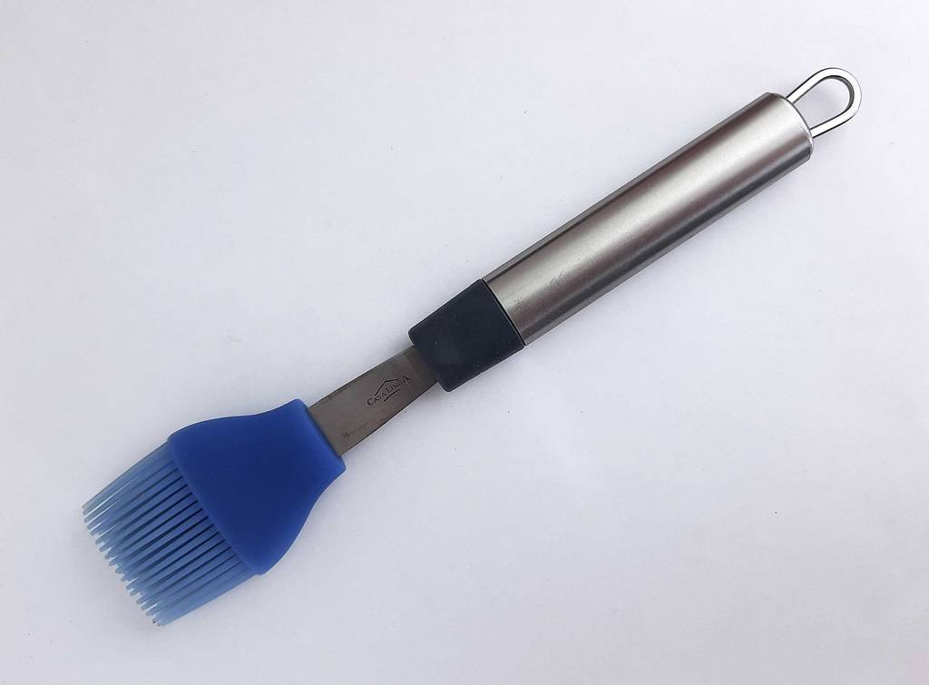 Der Grillpinsel im Test, inklusive eines violettfarbenen Silikon-Kopfes und eines Aluminiumgriffs, liegt von oben betrachtet auf einer weißen Oberfläche.