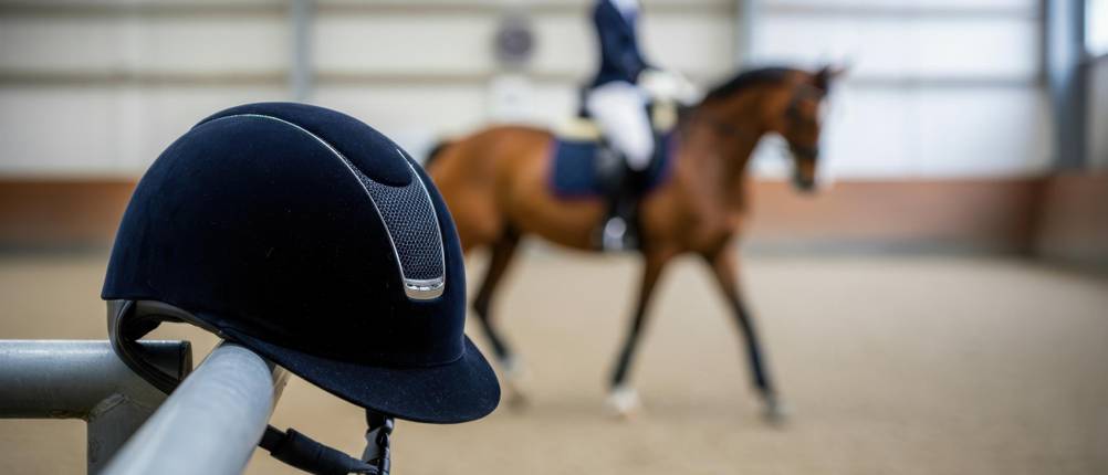 Casco-Reithelm-Test: Ein Helm in der Nahaufnahme vorn, eine Reiterin mit Pferd im Hintergrund.