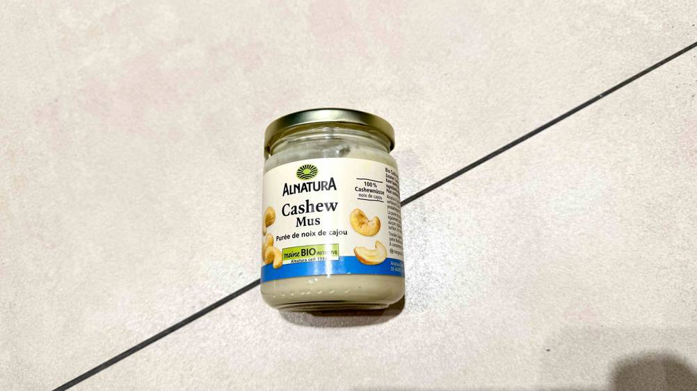 Auf einem hellen Boden liegt ein Glas des Cashewmus im Test.
