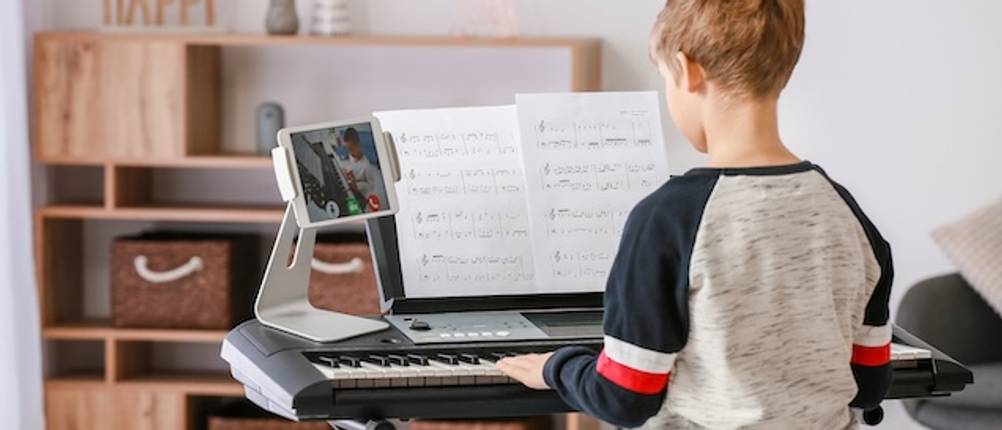 Casio-Keyboard von einem Jungen getestet: Das Kind sitzt vor einem Keyboard, das auf einem Keyboardständer abgestellt ist und spielt nach Noten.