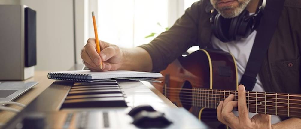Casio-Keyboard im Test: Ein Mann sitzt mit einer Gitarre neben einem Keyboard mit macht sich Notizen.