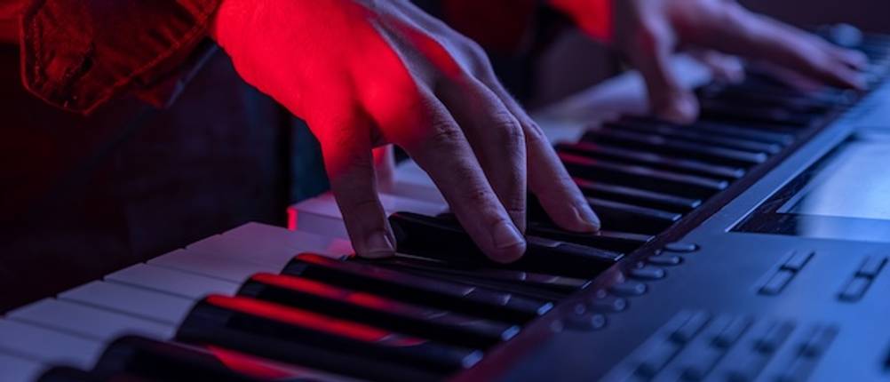 Casio-Keyboard im Test: Nahaufnahme von zwei Händen, die in einem dunklen Raum auf einem Keyboard spielen.