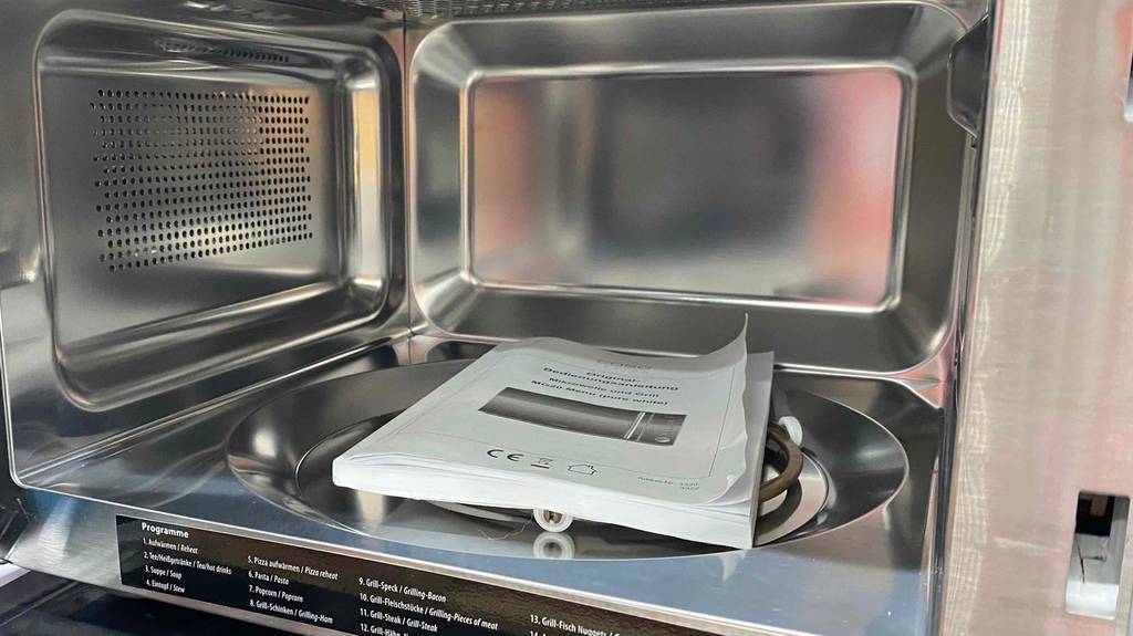 Mikrowelle, in der die Betriebsanleitung liegt, vorne sind verfügbare Programme aufgeklebt.