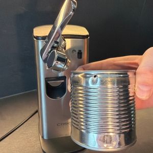 Eine Hand hält vor dem Caso-D10-Multiöffner eine Dose mit Loch fest