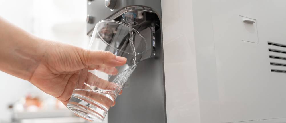 Eine Hand füllt mit einem Glas Wasser aus einer Maschine ab.