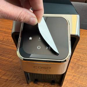 Eine Hand zieht einen Aufkleber vom Display des Caso HW 770 Advanced.