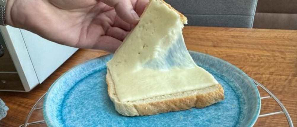 Eine Hand hält eine Scheibe Toast mit zerlaufenem Käse hoch