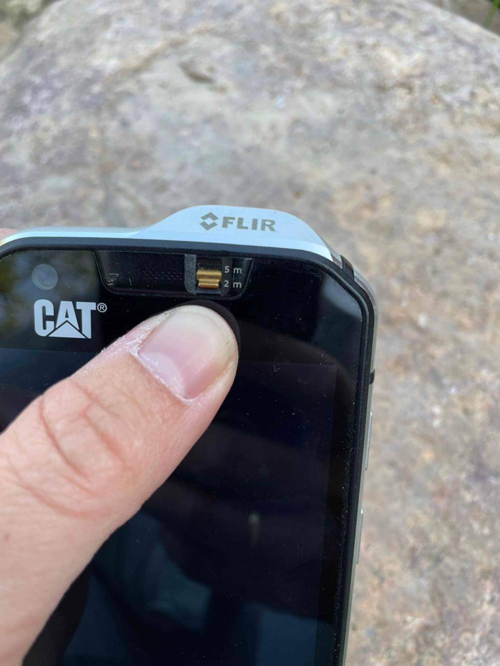 Ein Finger befindet sich an einem Umschalter eines getesteten Cat-Handys.