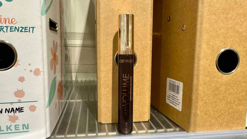 Ein Behälter Mascara braun steht zum testen vor einem Holzordner.
