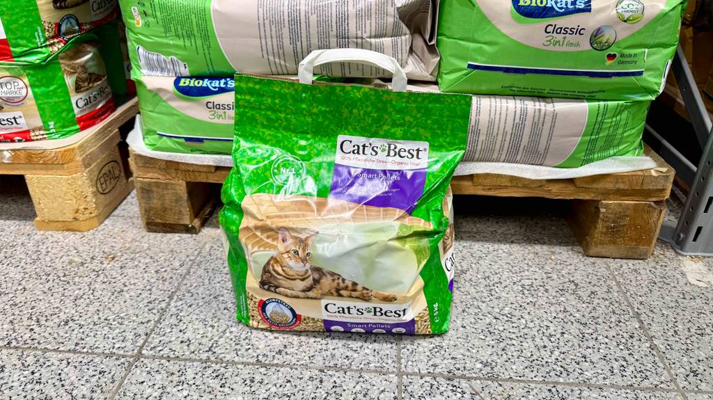Eine Packung Katzenstreu-Pellets steht zum testen vor anderen Packungen auf einem Fliesenboden.