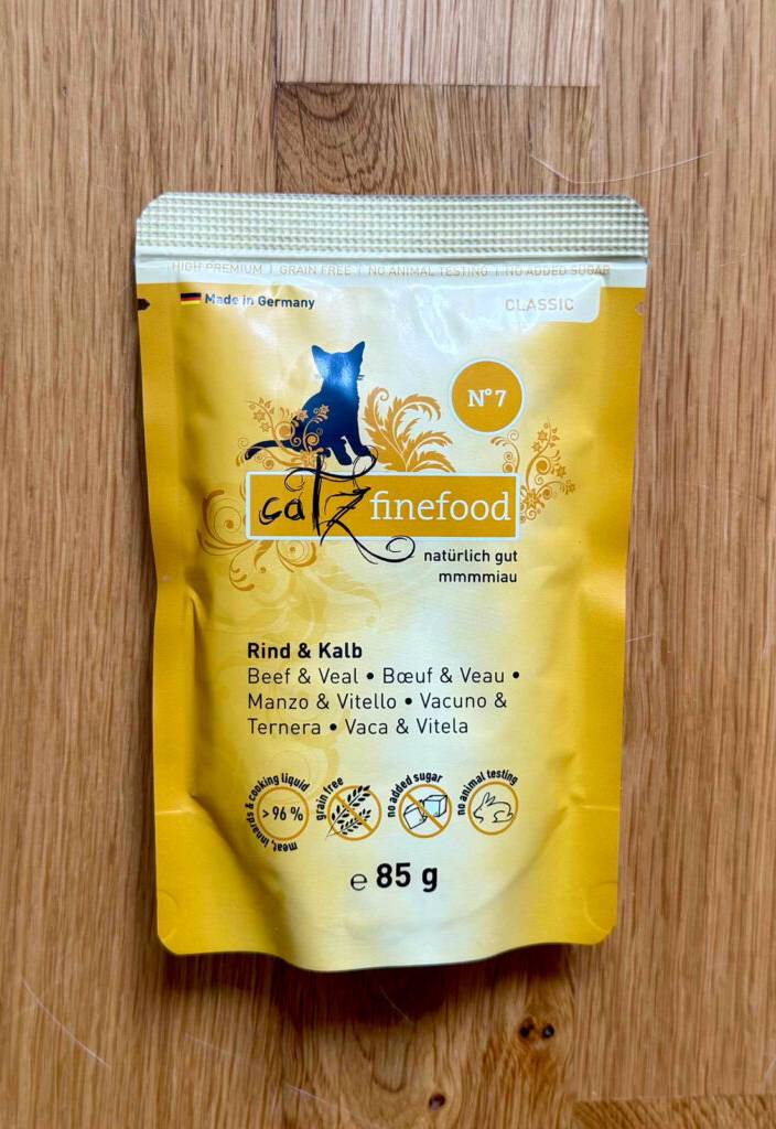 Katzenfutter ohne Zucker und Getreide im Test befindet sich in einem wiederverschließbaren 85-g-Beutel auf einer Holzfläche.