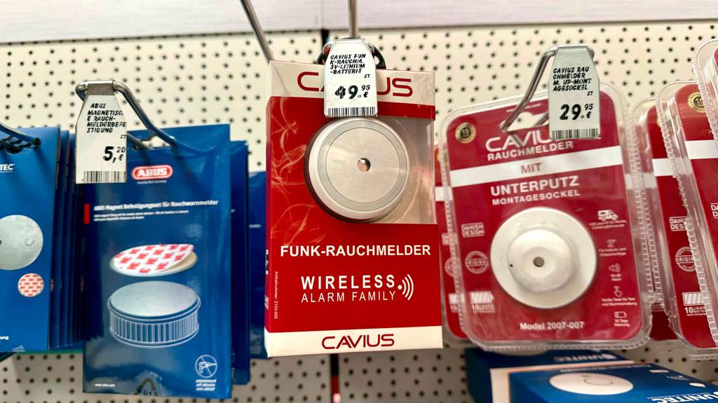 Rauchmelder ohne LED im Test: Ein verpacktes Gerät hängt zwischen anderen Produkten in einem Loch-Hängeregal.