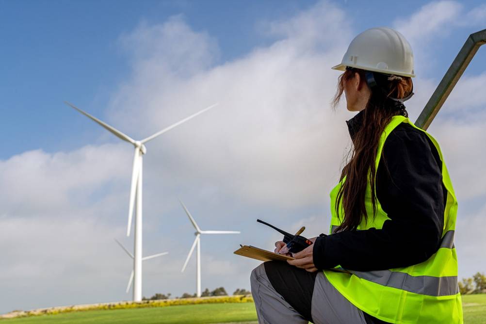 Eine Frau sitzt auf einem Feld mit einem getesteten CB-Handfunkgerät und sieht zu einem Windpark.