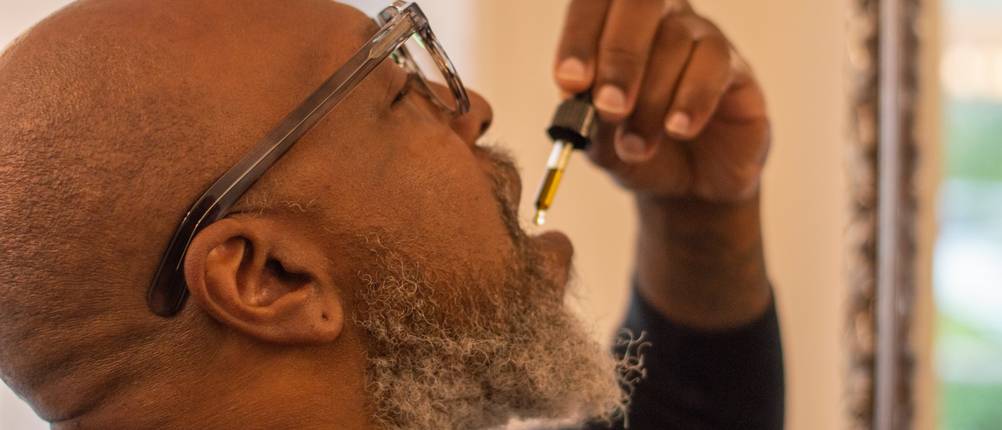 CBD-Öl kaufen: Ein Mann träufelt sich CBD-Öl unter die Zunge.