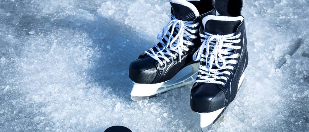 CCM-Schlittschuhe im Test: Ein Paar Schlittschuhe steht neben einem Puk auf dem Eis.