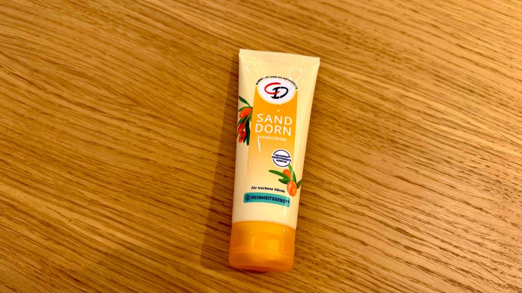 Eine Sanddorn-Handcreme liegt zum testen auf einer Holzfläche.