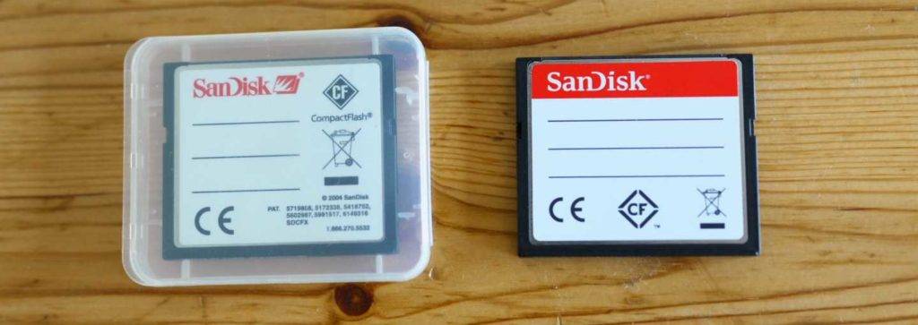 CF-Karten-Test: Zwei SanDisk Karten, davon eine im Kunststoffbehälter, mit weißen beschriftbaren Etiketten liegen nebeneinander auf einer Holzfläche.