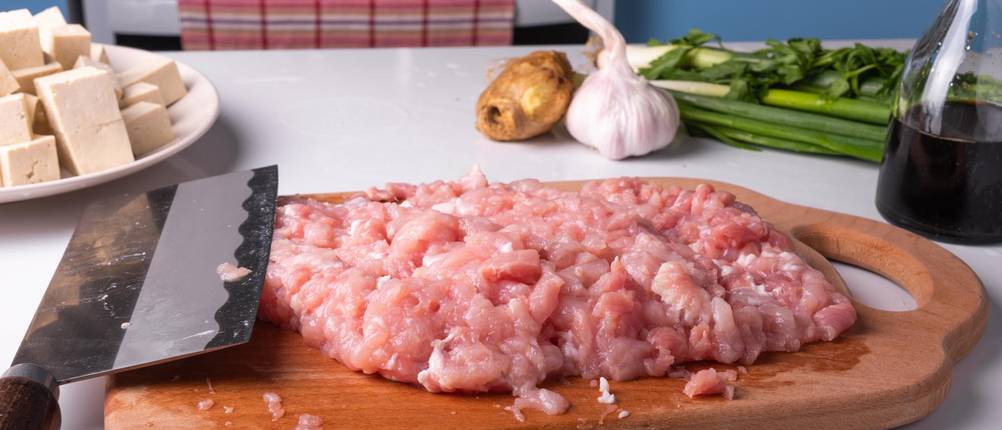 Chai-Dao-Messer-Test: Ein Chai-Dao-Messer liegt neben Hackfleisch auf einem Holzbrett.