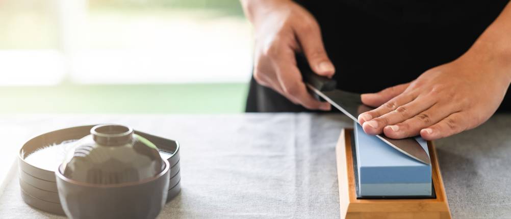 Chai-Dao-Messer-Test: Eine Hand führt ein Chai-Dao-Messer über einen Schleifstein.