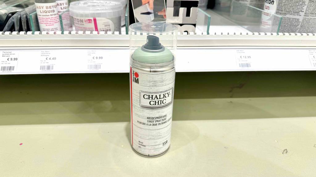 Kreidespray testen: Eine Spraydose steht vor einem Verkaufsregal mit Farbprodukten.