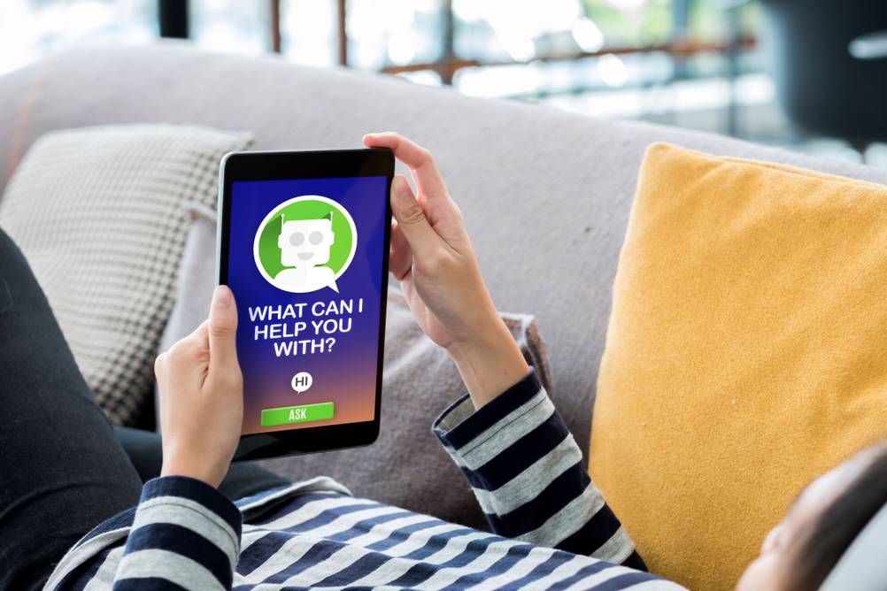 Eine Frau liegt auf dem Sofa und chattet mit einem Chatbot.