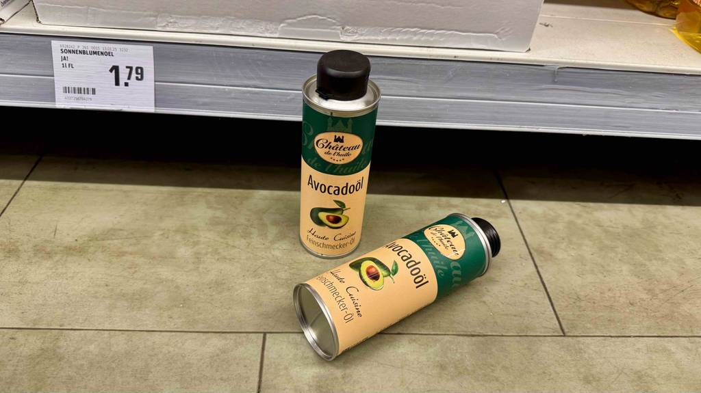 Zwei Aluminiumdosen mit getestetem Avocadoöl befinden sich auf dem Boden vor einem Verkaufsregal.