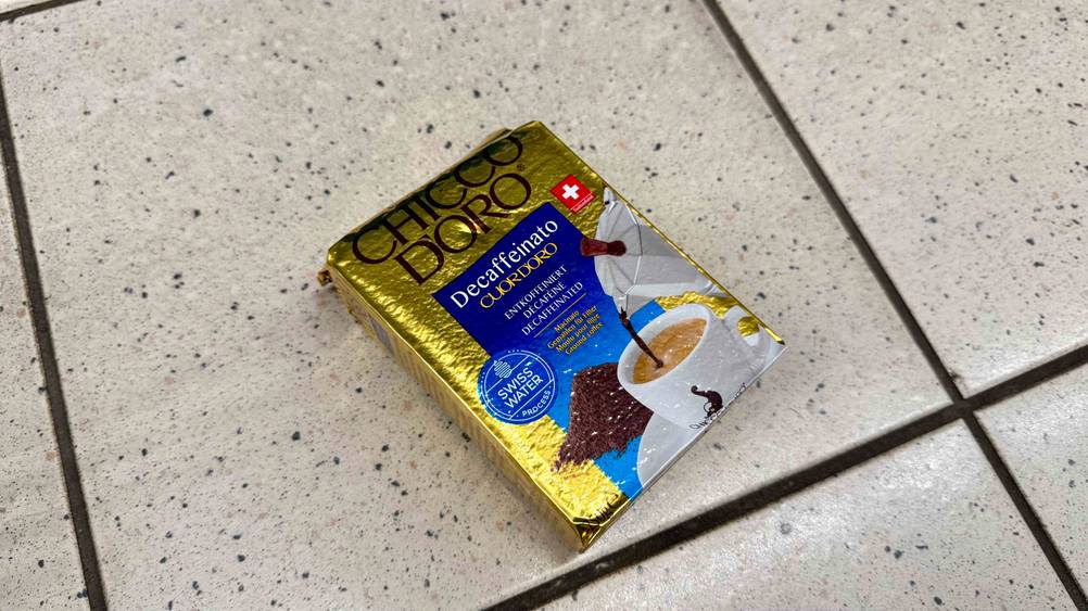 Auf dem Boden liegt leicht horizontal eine Packung des getesteten Chicco-d'Oro-Kaffees.