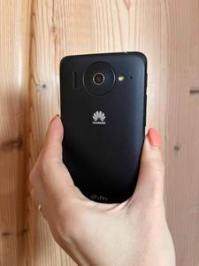 Eine Hand hält das getestete China-Handy vor eine Holzwand, Fokus auf die Kamera.