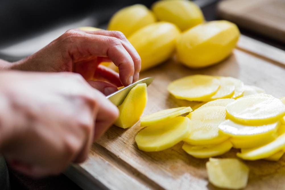 Chipsmaker-Mikrowelle-Test: Jemand schneidet Kartoffeln, Kartoffelscheiben liegen auf einem Holzbrett.