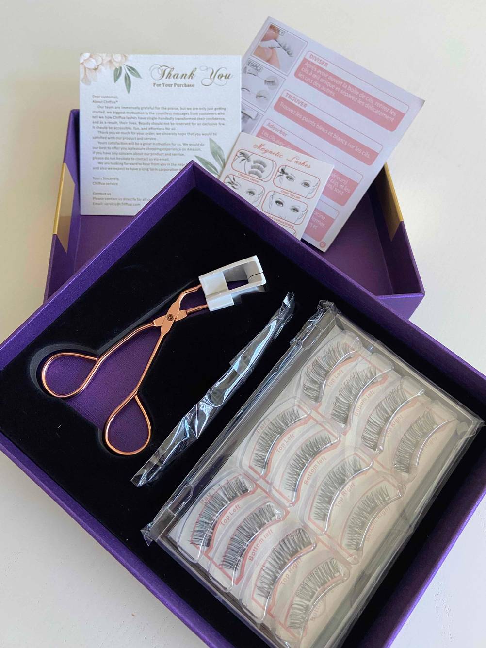 Eine geöffnete schwarz-violette Geschenkverpackung mit magnetischen Wimpern im Test inklusive Pinzette und weiterem Zubehör, von oben betrachtet vor einem weißen Hintergrund.