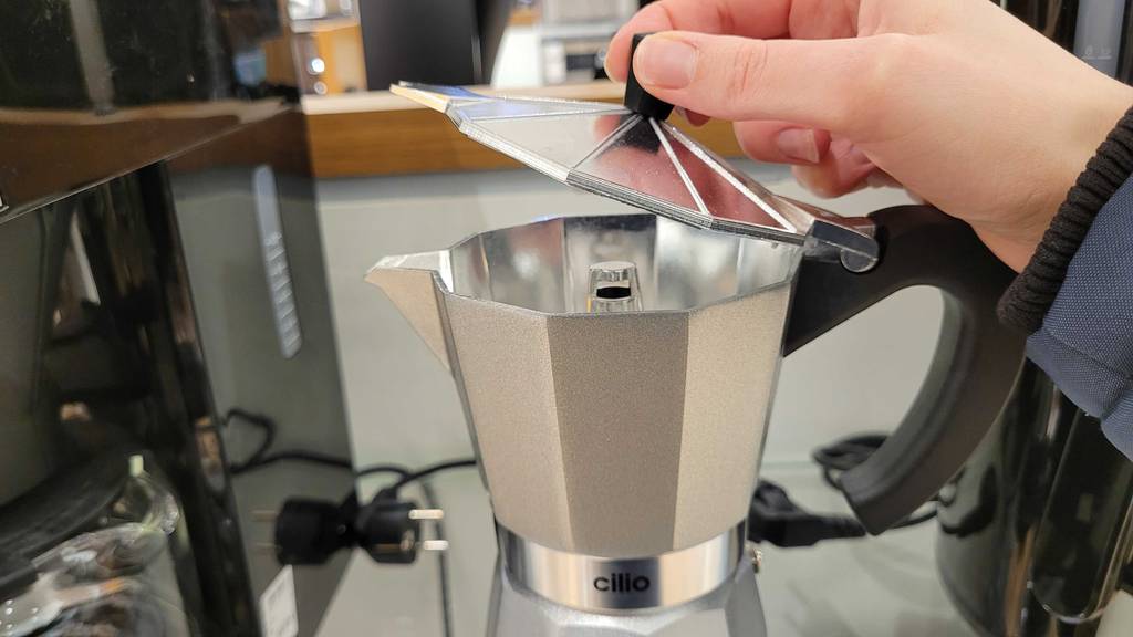 Hand öffnet den Deckel eines getesteten Espressokochers elektrisch.