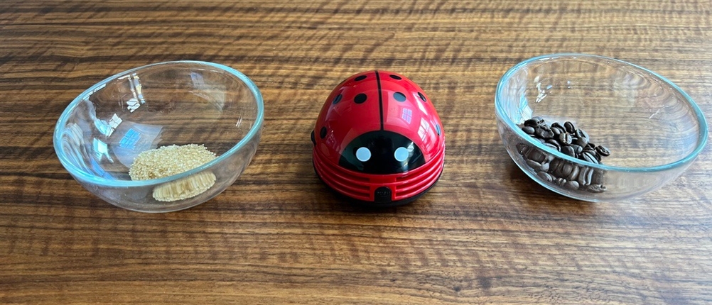 Tischstaubsauger in der Mitte, rechts und links Glasschalen mit Zucker und Kaffeebohnen.