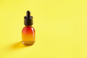 Glass bottle for cosmetics, serums and oils with a pipette on a yellow background