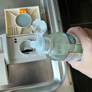 Eine Hand hält einen Klarspüler über den dafür vorgesehenen Einlass in der Spülmaschine