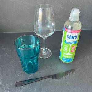 Neben dem Claro-Öko-Klarspüler stehen ein Weinglas, ein Glas und ein Messer